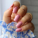 Close-up of a hand with pink nail polish and gold rings on a neutral background, Obroi