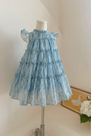 Blue tiered dress on a mannequin against a neutral background with flowers, Obroi