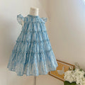 Blue tiered dress on a mannequin against a neutral background with flowers, Obroi