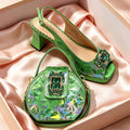A green geometric-patterned shoe and matching handbag displayed in a pink box lined with satin fabric. The shoe is a slingback high-heel with a jeweled embellishment on the toe, and the bag is a small round handbag with a matching strap and front clasp, Obroi