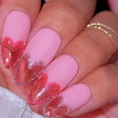 Close-up of a hand with pink nails featuring red heart designs, Obroi