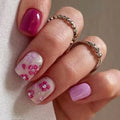 Hand with pink and white floral nail design on a neutral background, Obroi