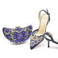 Navy high-heeled shoes with blue gemstones and a matching clutch on a white background, Obroi