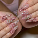 Close-up of hands with long, pointed stiletto nails decorated with pink glitter, white swirls, rhinestones, and silver crescent moon and star charms, Obroi