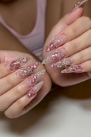 Close-up of hands with long, pointed stiletto nails decorated with pink glitter, white swirls, rhinestones, and silver crescent moon and star charms, Obroi