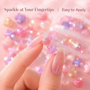 A close-up of a hand with long pink manicured nails holding two small glittery star-shaped nail art charms, with more pink heart and star charms and a clear container blurred in the background. Text at the top reads 'Sparkle at Your Fingertips | Easy to Apply', Obroi