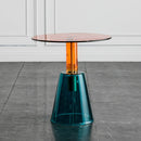 Modern side table with a transparent glass top and teal base on a gray floor, Obroi