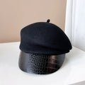 Black beret on a textured black base against a beige wall, Obroi