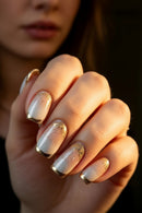 A close-up of a hand with elegant French tip manicure nails featuring a glossy white base, a soft champagne-gold gradient, and scattered gold glitter, Obroi
