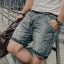 Person wearing denim shorts and a white shirt, holding a brown leather bag.