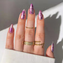 Hand with purple and clear nail polish wearing gold rings on a neutral background, Obroi