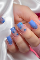 Hand with blue gradient nails featuring glitter and small decorative elements on a white background, Obroi