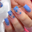 Hand with blue nail polish featuring butterfly designs on a white background, Obroi