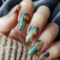 Close-up of hands with teal and gold nail art on a textured fabric background, Obroi