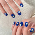 Blue nail polish with white daisy designs on a neutral background, Obroi