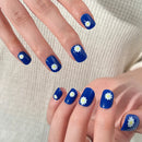 Blue nail polish with white daisy designs on a neutral background, Obroi