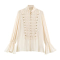 An off-white long-sleeve blouse with a high mock neck, pleated front panel, decorative cord details with gold-tone buttons, and flared bell sleeves, shown on a plain white background, Obroi