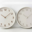 Two minimalist round wall clocks with a matte off-white finish, featuring raised numerals and slim hands, displayed side-by-side against a clean white background, Obroi