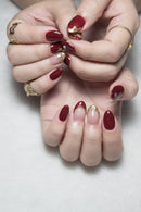 Close-up of hands with red nail polish and gold accents on a neutral background, Obroi