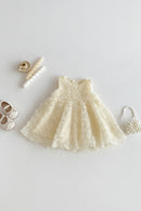 Cream-colored lace dress with baby shoes, headband, and rattle on a white background, Obroi