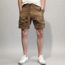 Person wearing brown cargo shorts and white sneakers against a white background, Obroi