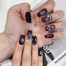 Hand with dark purple nail polish featuring decorative patterns on a white background, Obroi