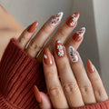 Nails with floral and leaf designs in a warm color palette, Obroi