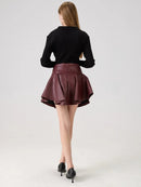 Person wearing a black top and burgundy leather skirt on a white background, Obroi