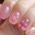 Close-up of a hand with pink nail art featuring hearts and plaid patterns, Obroi