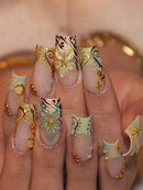Nails with decorative butterfly design in gold, black, and white on a neutral background, Obroi