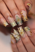 Nails with decorative butterfly design in gold, black, and white on a neutral background, Obroi