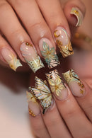 Nails with decorative butterfly design in gold, black, and white on a neutral background, Obroi