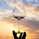 Clear wine glass held against a sunset sky, Obroi