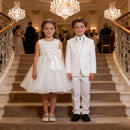 Two children in formal attire standing on a staircase in an elegant indoor setting, Obroi