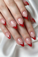 A close-up of a hand with long stiletto-shaped nails featuring a glossy nude-pink base, bright red tips, and a small silver rhinestone V-accent near the cuticle, Obroi