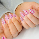 Close-up of a hand with pink and green plaid nail design on a neutral background, Obroi