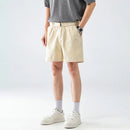 Person wearing beige shorts and white sneakers on a plain background, Obroi
