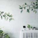 Decorative wall stickers of green leaves on a light gray wall with a white crib and small plants, Obroi
