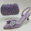 Purple high-heeled shoe with decorative bow and matching clutch on a white background, Obroi