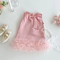 Pink dress with a bow and ruffles on a light gray surface, surrounded by shoes and a teddy bear, Obroi