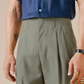 Person wearing a blue shirt and green pleated pants on a beige background, Obroi