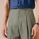 Person wearing a blue shirt and green pleated pants on a beige background, Obroi