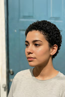 Woman with short curly hair wearing a gray shirt against a blue door, Obroi