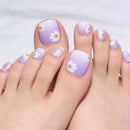 Close-up of a person's feet with manicured toenails featuring a lavender-to-white gradient, white daisy floral designs, and silver glitter accents, Obroi