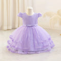A lavender purple toddler girl's party dress displayed on a mannequin. The dress features a textured honeycomb lace bodice, short puff sleeves, a matching waist bow, and a tiered tulle skirt with lace trim.