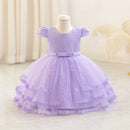A lavender purple toddler girl's party dress displayed on a mannequin. The dress features a textured honeycomb lace bodice, short puff sleeves, a matching waist bow, and a tiered tulle skirt with lace trim.
