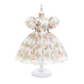 A white toddler girl's dress with a pink and green floral print, featuring puffy short sleeves and a full skirt, displayed on a white mannequin dress form against a white background, Obroi