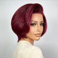 A woman wearing a short, voluminous bob wig in a rich deep burgundy shade, photographed against a neutral light gray background, Obroi