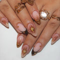 Close-up of hands with pink nail polish and gold decorations, wearing multiple rings, Obroi