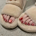 Beige slippers worn with toes showing and red nail polish on a neutral background, Obroi